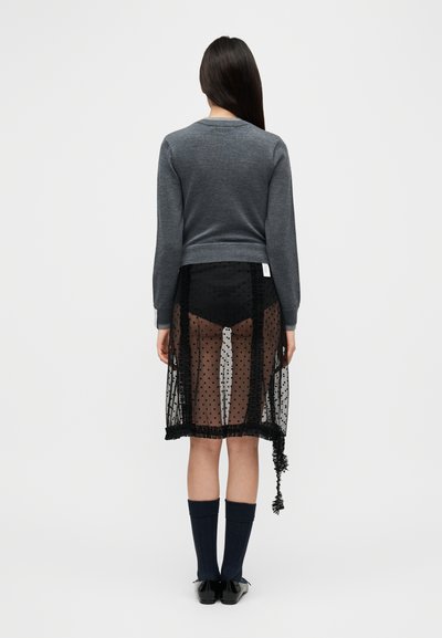 Γκρι πλεκτό πουλόβερ, μαύρη διάφανη φούστα με πουά και βολάν στο τελείωμα, μπλε μέχρι το γόνατο κάλτσες και μαύρα παπούτσια. Ορατά υλικά με υφή.