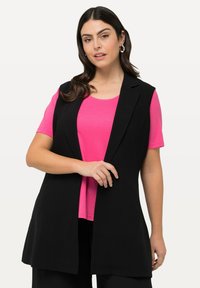 Blazer senza maniche nero con colletto a scialle sopra una t-shirt rosa brillante. Il tessuto appare liscio, con linee pulite e una vestibilità rilassata.