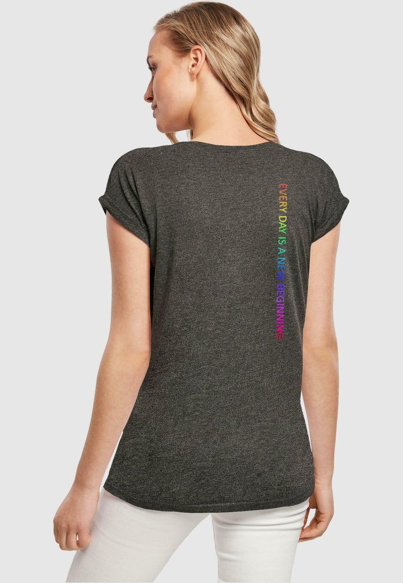 Graues T-Shirt mit kurz ausgefallenen Ärmeln, das auf der Rückseite mehrfarbigen Text trägt, der "JEDER TAG IST EIN NEUER BEGINN" liest. Glatte Textur.