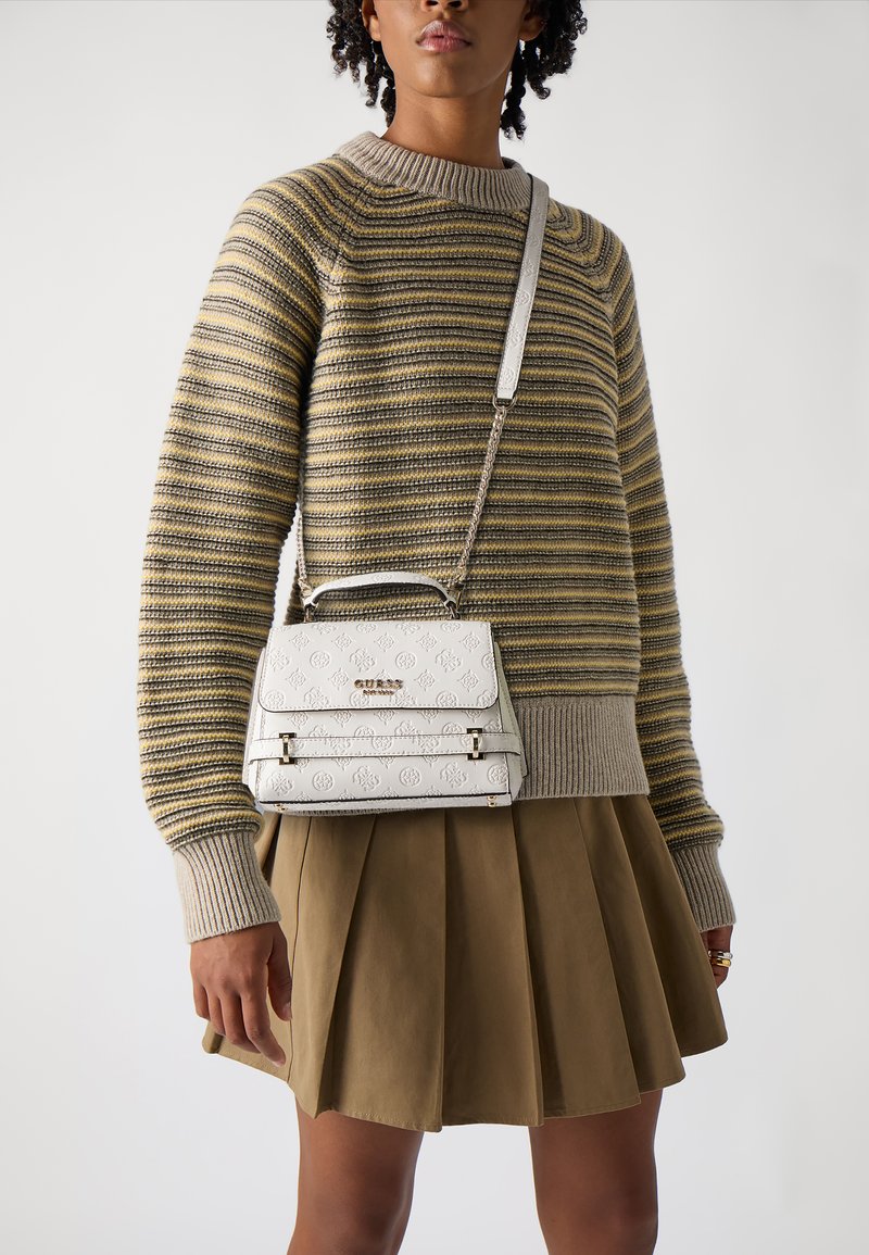 Borsa bianca con rilievi e forma strutturata, hardware dorato a contrasto e tracolla a catena, indossata sopra un maglione a righe e una gonna color khaki.