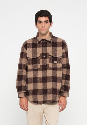 Brown and tan plaid flannel shirt with a button-up front, two chest pockets, and a tag on the left side. Soft texture with a relaxed fit.
