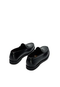 Ζευγάρι μαύρα δερμάτινα ανδρικά μοκασίνια χωρίς κορδόνια με χαμηλά τακούνια, εμφανιζόμενα σε λευκό φόντο, σε γωνία που δείχνει την πίσω και την πάνω πλευρά.