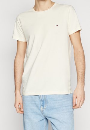 Light beige cotton T-shirt with short sleeves and a round neckline. Features a small logo on the left chest. Smooth texture.