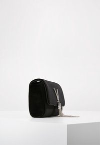 Black rectangular handbag with flap closure, silver "V" logo, and silver chain tassel, placed on a white surface against a plain background.