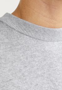 Grijze gebreide trui met een geribbelde ronde hals, die een zachte textuur heeft en een close-up weergave biedt van de weving en stikseldetails van de stof.