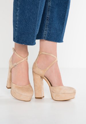Voeten met beige suède plateauhakken met enkelbandjes en brede blokhakken, gecombineerd met cropped blauwe spijkerbroeken.