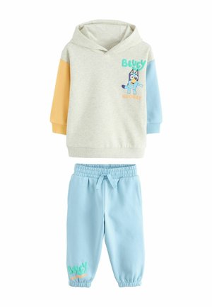 Baumwoll-Trainingsanzug mit einer hellgrauen Kapuzenjacke, die orangefarbene und blaue Ärmel hat, sowie blauen Jogginghosen mit elastischem Bund und Textakzenten.