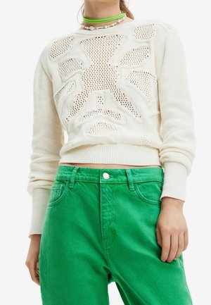 Hvid strikket sweater med geometrisk hulmønster, kombineret med lysegrønne højttaljede bukser og lagdelte grønne og perle halskæder.