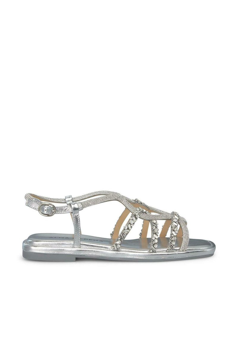 Sandalias planas plateadas con cierre de tira, que presentan adornos de cuentas decorativas y múltiples tiras entrecruzadas. Acabado metálico suave, diseño de punta abierta.