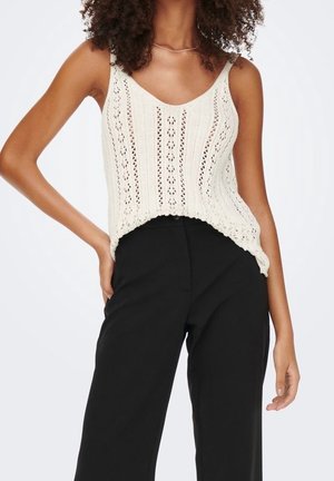 Top de punto en blanco roto con patrón de calado vertical y dobladillo con volantes, combinado con pantalones de pierna ancha negros de talle alto.
