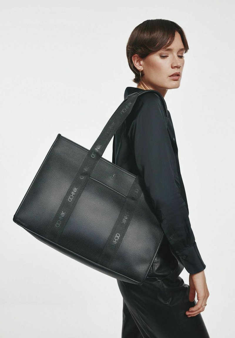Czarna torba na ramię wykonana z teksturowanego materiału, o prostokątnym kształcie, z podwójnymi uchwytami i kontrastowymi paskami z logo.