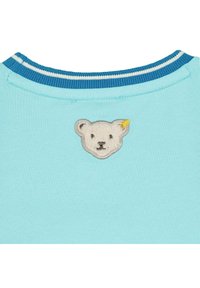 Camiseta de algodón azul claro con cuello redondo y rayas azules y blancas. Decorada con la cara de un oso bordada y fuzzy en el pecho.