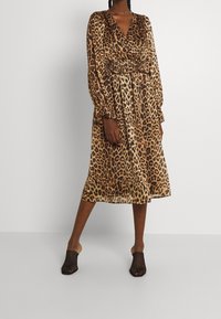 Leopardmönstrad omslagsklänning med långa ärmar och sammanknuten midja. Tillverkad av lätt tyg, midilängd, matchad med svarta sandaler med öppen tå och nät.