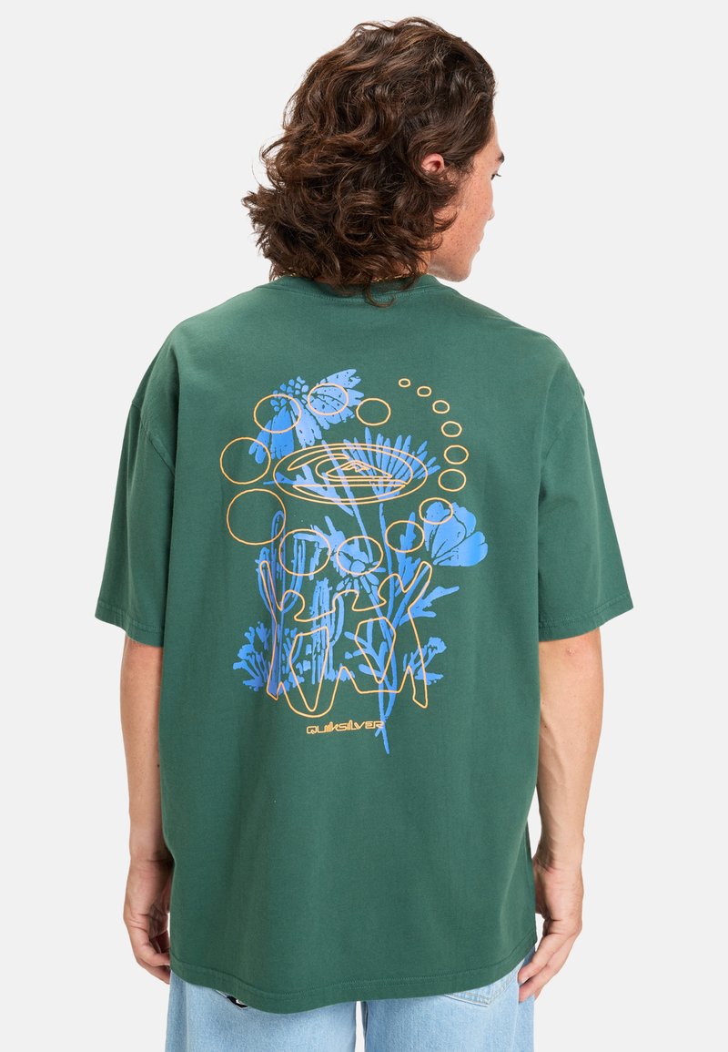 Camiseta de algodón verde con un corte holgado. Presenta un diseño colorido de flores y abstracto en azul y naranja en la parte posterior. Mangas cortas.