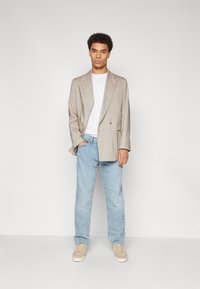 Beige linen blazer with a double-breasted design, paired with a white t-shirt and light blue denim jeans. Beige sneakers complete the look.