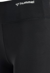Leggings de sport noirs avec une texture lisse et extensible. Comprend une large ceinture et un petit logo en haut. Design sans couture pour plus de confort.