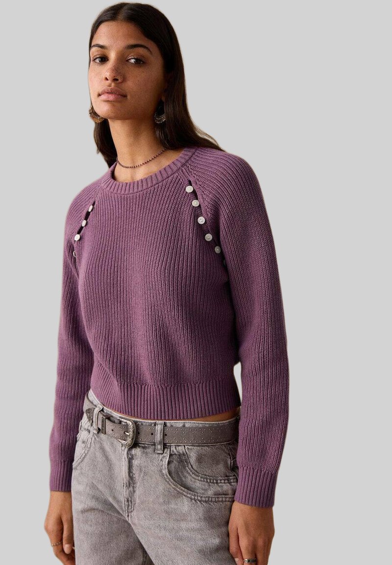 Pull violet tricoté avec texture côtelée, encolure ronde et boutons décoratifs sur les épaules. Design court.