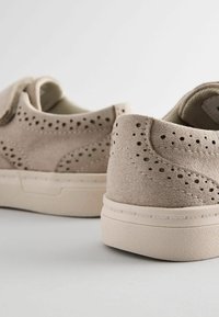 Beige canvas sneakers feature perforated details, a textured finish, and a rubber sole with a simple design. Back view shows soft contours.