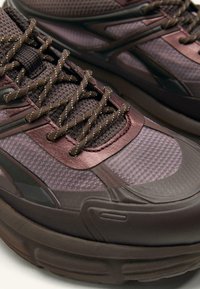 Purple and brown athletic shoes feature a mesh upper with metallic accents, textured laces, and a thick rubber sole for cushioning.