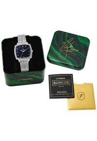 Montre Fossil avec bracelet en métal argenté et cadran carré bleu marine ornés d'un motif étoilé. Livrée dans une boîte en métal verte à motifs tourbillonnants avec une signature et des cartes.