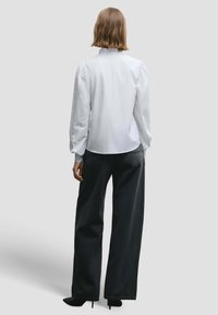 White long-sleeve shirt with a high collar, paired with loose black jeans, featuring a clean design and smooth texture. Black heels complete the look.
