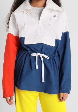 Farveblokkeret anorak-jakke i hvid, rød og blå. Har en halv-zip foran, snoretræk i taljen og elastiske manchetter. Blødt materiale.