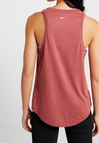 Camiseta atlética sin mangas de color rojo, hecha de un tejido suave, con un dobladillo curvado y un pequeño logo de Nike en la parte superior de la espalda.