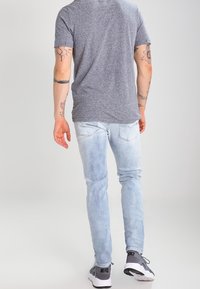 Šedé tričko s krátkým rukávem, světle modré džíny s úzkým střihem a černobílé sportovní tenisky s viditelným logem. Úzký střih přiléhající k tělu.