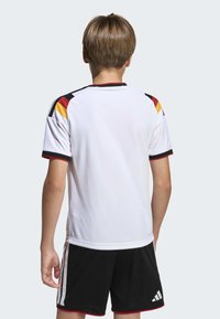 White sports jersey featuring black, red, and yellow accents along the shoulders and sleeves, paired with black shorts with white stripes.