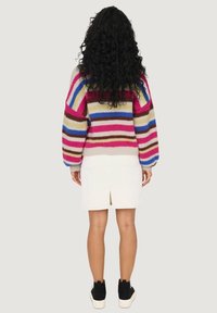 Maglione lavorato a maglia con righe orizzontali in rosa, blu e beige. Vestibilità ampia, maniche a palloncino, abbinato a una gonna bianca e scarpe nere.
