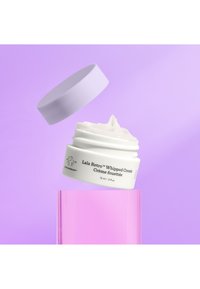 White jar of Lala Retro Whipped Cream with a lilac lid, showcasing creamy texture, labeled with product information, against a soft purple background.