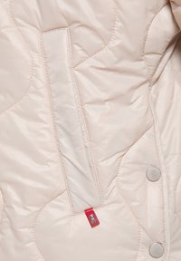 Lichtroze gewatteerde jas met een zijzak, zilveren drukknoopjes en een klein rood logo-tag. Glad, glanzend stof met een zachte textuur.