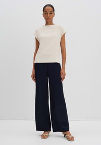 Beige textured top with cap sleeves paired with high-waisted navy wide-leg pants. Model wears sandals with a minimal design.