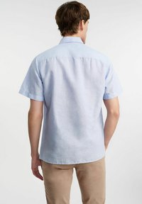 Jasnoniebieska koszula z krótkim rękawem, wykonana z miękkiego materiału, z kołnierzykiem zapinanym na guziki, charakteryzująca się gładką fakturą i prostym dołem.