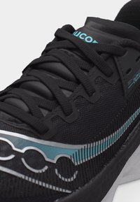 Μαύρο αθλητικό παπούτσι με μαύρα κορδόνια, επάνω μέρος από δίχτυ, ρίγα μάρκας σε τιρκουάζ και ασημί, και απορρόφηση κραδασμών σε λευκή σόλα.