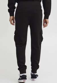 Zwarte sweatpants gemaakt van een zachte stof, met zijvakjes en geribbelde boorden. Gecombineerd met zwarte sneakers en witte enkelsokken.
