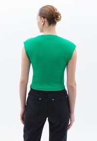 Zelený žebrovaný tílko s krátkými rukávy, kombinované s černými džínami s vysokým pasem, které mají zadní kapsy a kovové detaily.