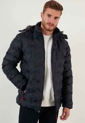 Dunkelblauer Pufferjacke mit gestepptem Muster, ausgestattet mit einem Reißverschluss, Kapuze mit Kunstfellbesatz und roten Reißverschlussakzenten.