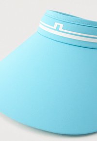 Svetlo modra sončna kapa s belim pasom in geometrijskim vzorcem okoli traku, izolirana na enobarvni podlagi.