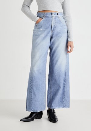 Jasnoniebieskie jeansy typu wide-leg wykonane z denimu z wysokim stanem, z dwoma przednimi kieszeniami i subtelnymi szczegółami blaknięcia. Połączone z czarnymi botkami za kostkę.