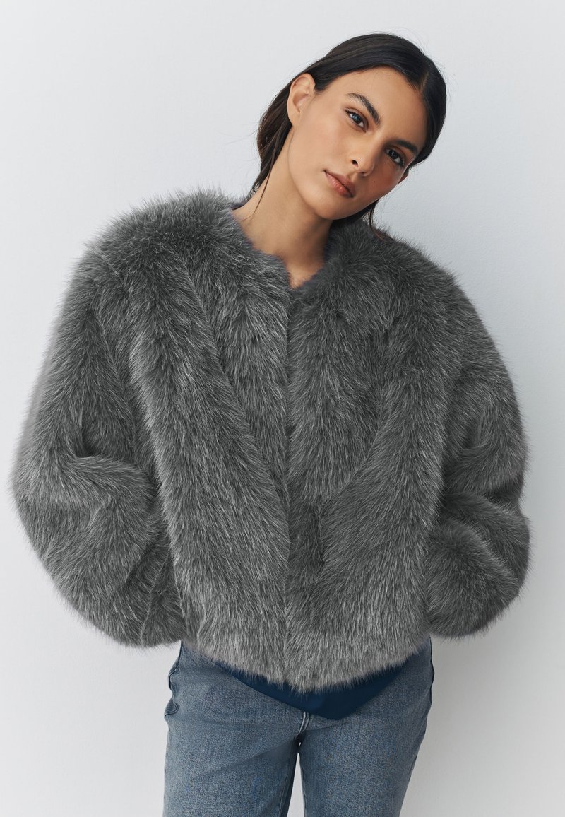Gray faux fur jacket with wide sleeves, a rounded collar, and a soft texture, paired with blue denim jeans.