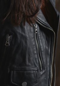 Czarna skórzana kurtka z srebrnymi zamkami błyskawicznymi, z boczną kieszenią oraz zbliżeniem na fakturę materiału i detale szwów.