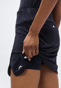 Ναυτικό αθλητικό φόρεμα με υφασμένες ρίγες, που διαθέτει κρυφή τσέπη και λευκή διακριτική λογότυπο. Κατασκευασμένο από ελαστικό, υλικό που απομακρύνει την υγρασία.