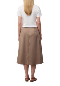 Een vrouw die een aansluitend wit T-shirt en een beige rok tot de knie draagt, met een gladde stofstructuur en een eenvoudig ontwerp, gecombineerd met bruine sandalen.