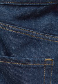 Close-up van donkerblauwe denimstof met gedetailleerde gele stiksels en een zaknaad.