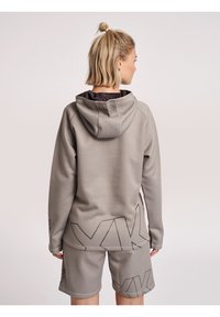 Pullover grigio con cappuccio e accenti geometrici neri, abbinato a pantaloni corti coordinati. Il tessuto sembra strutturato e morbido.