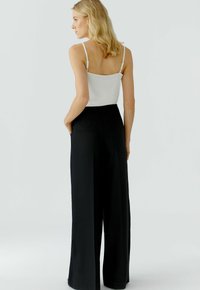 Pantalons larges noirs avec une taille haute, associés à un débardeur blanc. Les pantalons comportent des poches arrière et un tissu lisse.