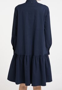 Abito blu navy con colletto abbottonato, maniche lunghe e orlo a balze stratificate. Realizzato in un tessuto morbido, presenta una vestibilità comoda.