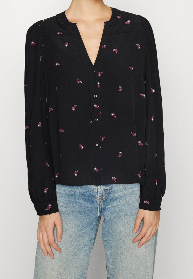 Blouse noire à manches longues bouffantes, décolleté en V, fermeture par boutons et motif paisley rose. Texture lisse avec des détails de col volanté.