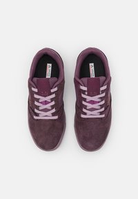 Sneaker in camoscio viola con punta arrotondata, lacci rosa e dettagli in rete. Etichetta del marchio visibile sulla linguetta. Texture morbida e design casual.